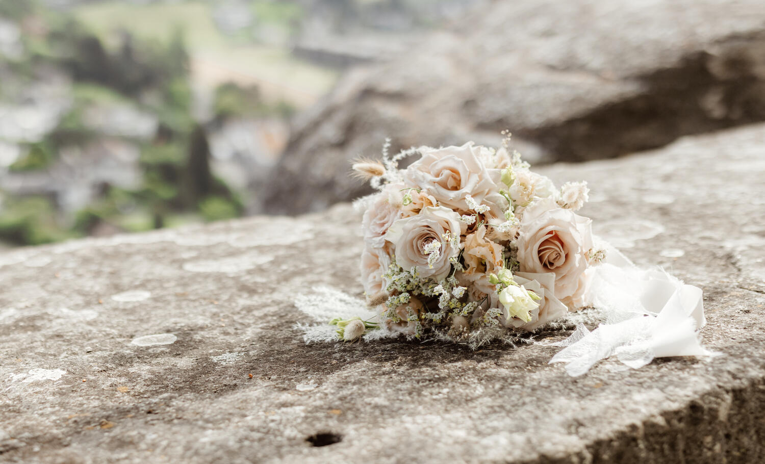 Ein Foto von einem Brautstrauss auf einer Steinwand. Der Braustrauss ist altrosa und weiss